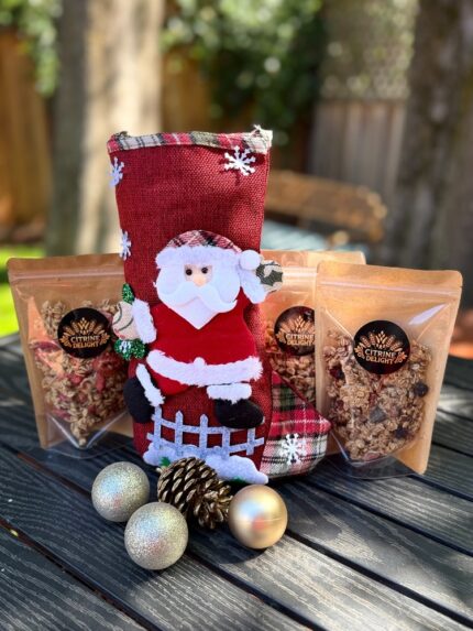 Santa stocking gift set with three Citrine Delight granola pouches and holiday ornaments on a picnic table.